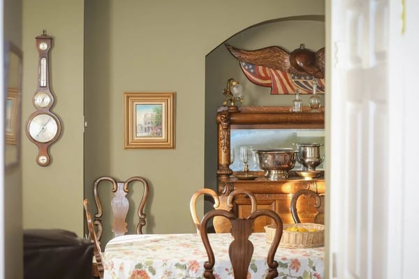 Bedroom with wrought-iron bed, white linens, ceiling fan, large windows with curtains, hardwood floors, and patterned area rug